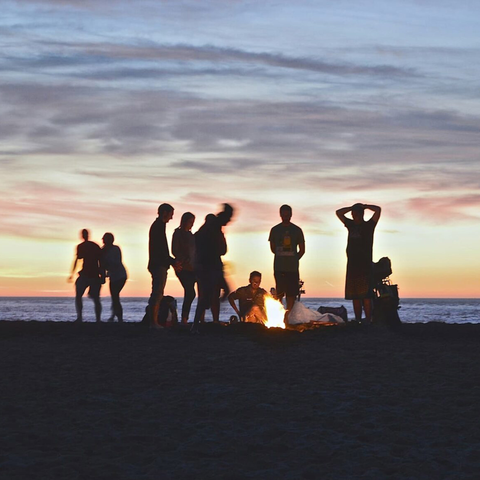 Persone attorno a un falò al tramonto sulla spiaggia, simbolo della collaborazione tra team e clienti per la gestione autonoma del sito WordPress